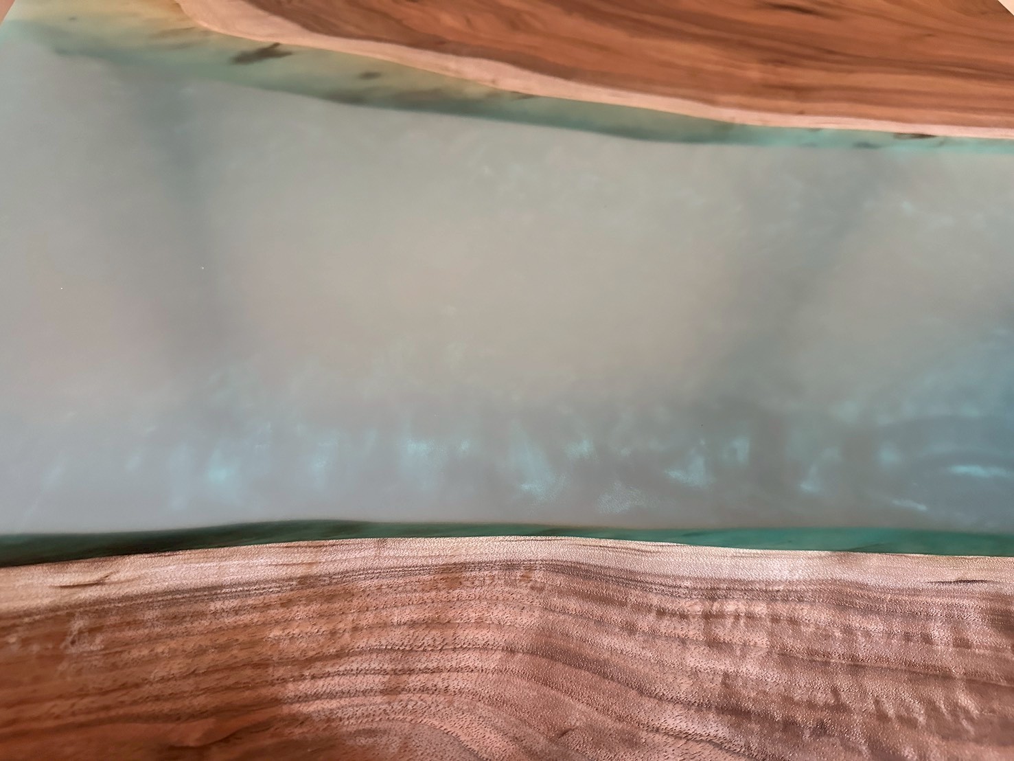 淡い水色のレジンと、波打つような木目が特徴的な天然木テーブルのクローズアップ