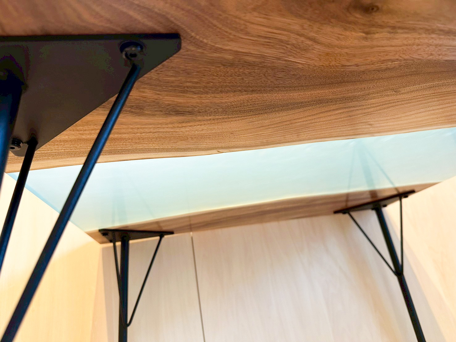 テーブルの下から見上げた、光を透過する薄い水色のレジン天板と木の質感のコントラスト