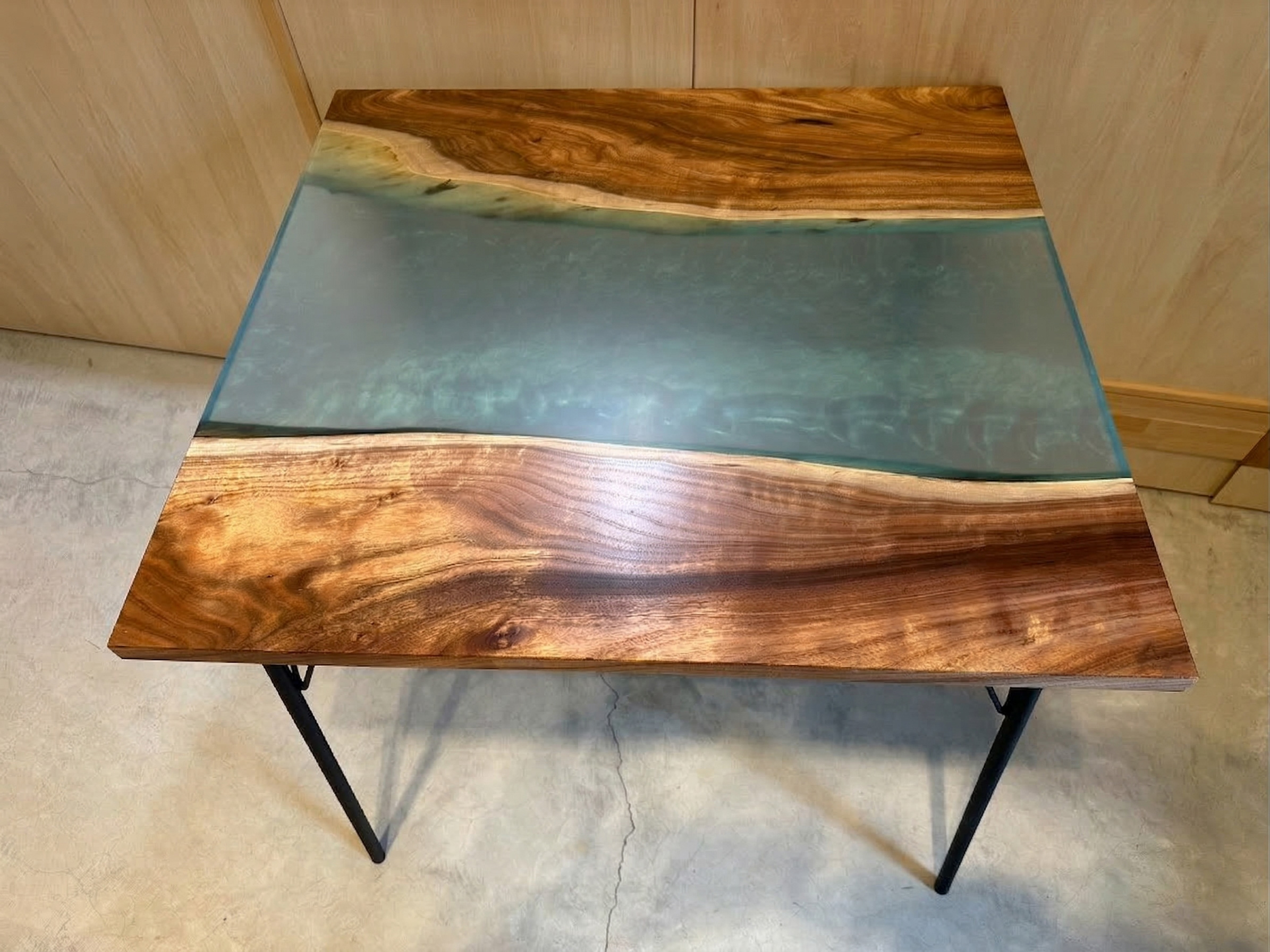 深みのある茶色の天然木と、波のような模様が入ったエメラルドグリーンのレジンを組み合わせたテーブルの正面写真